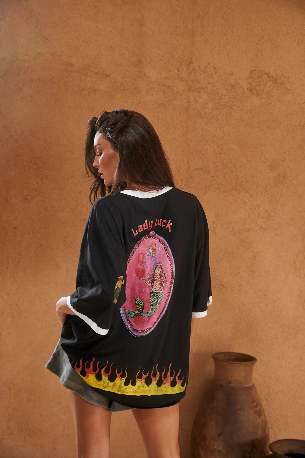 model draagt the lucky mermaid tee, achterkant met speelkaart print en vlammen onderaan