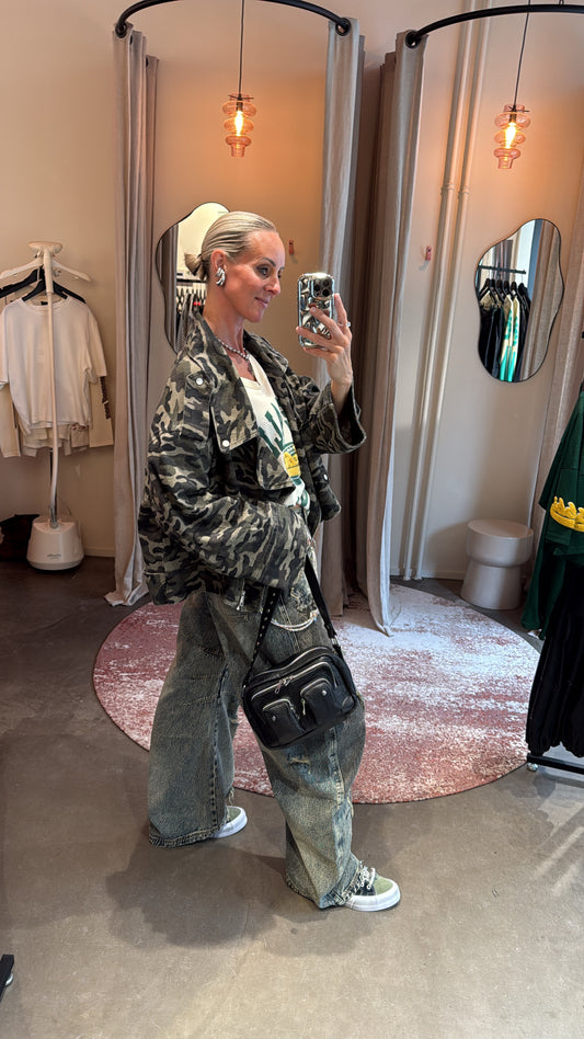 model draagt oversized camo jacket zijwaarts, gecombineerd met crossbody tas en wide leg jeans