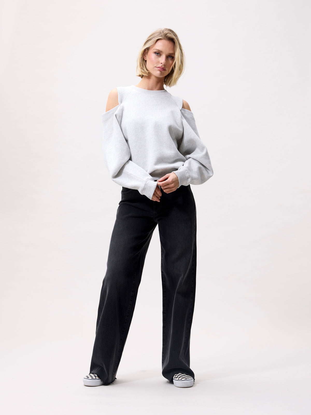 model in relaxed fit sweater met cut outs, volledige look met zwarte broek en sneakers