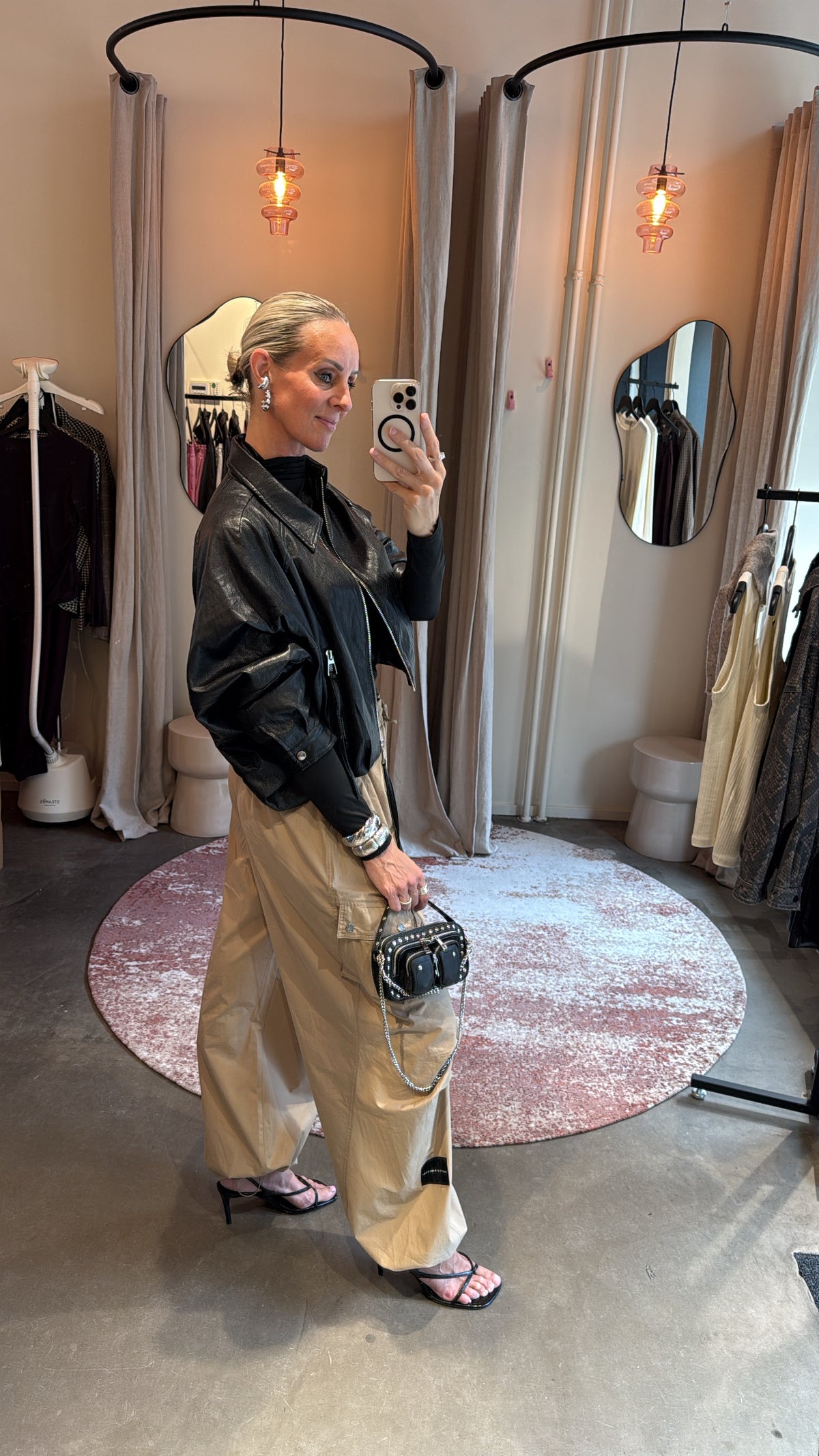 zijaanzicht van model in zwart vegan leren jack, gecombineerd met beige broek