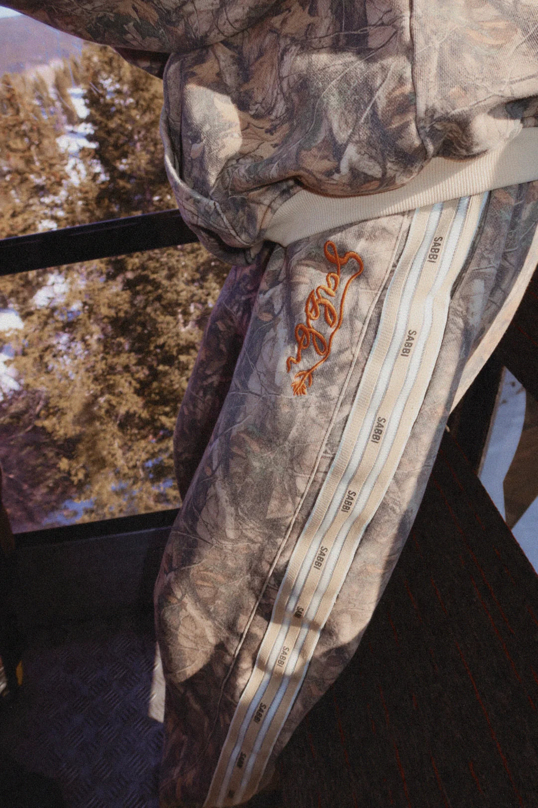 detail van zijstreep met sabbi logo en geborduurde tekst op de camo trackpants