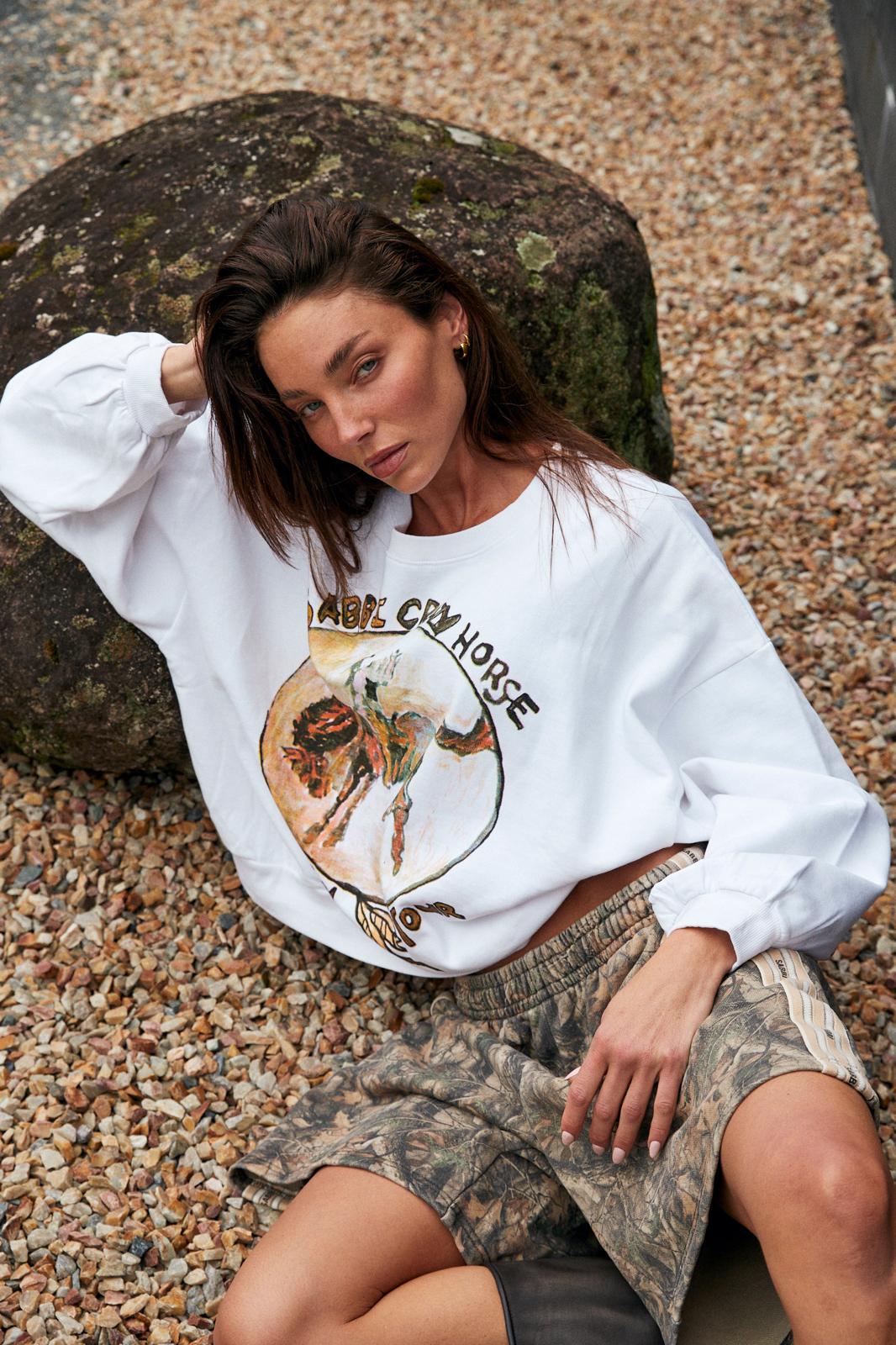 model zittend op grind draagt cali jumper gecombineerd met camo rok