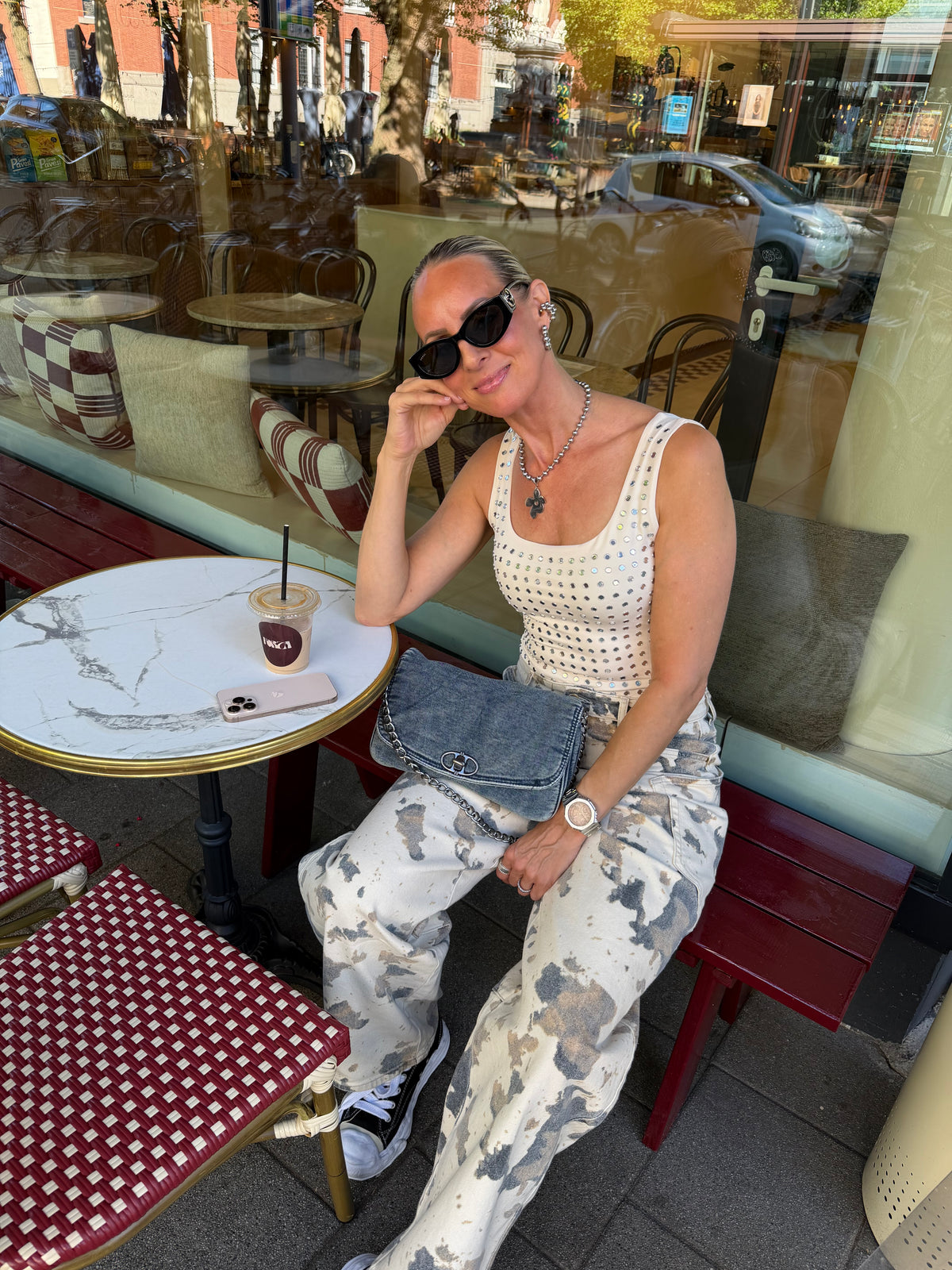 model draagt body eyelets champagne gecombineerd met print broek, zittend op terras