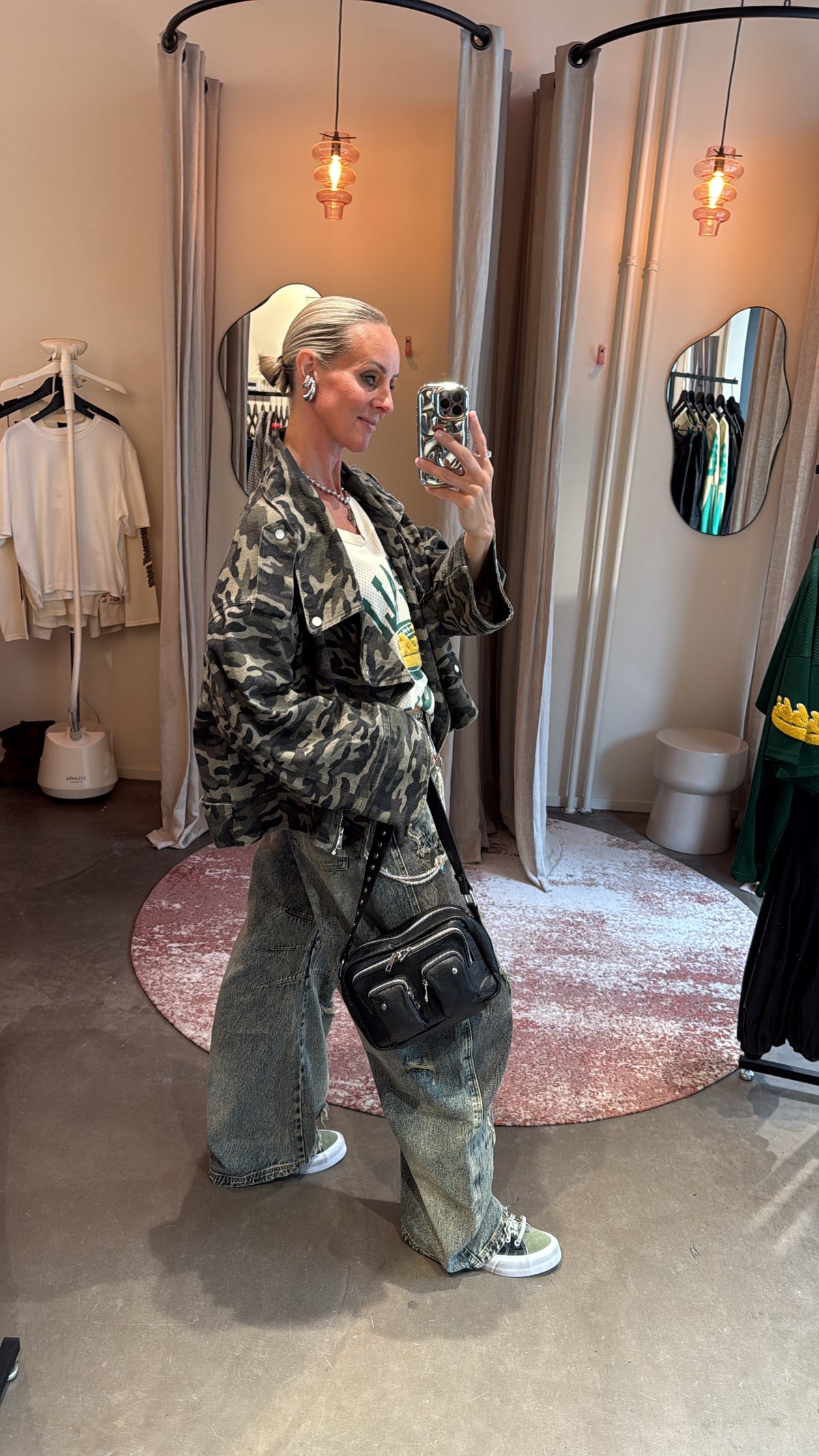 model draagt oversized camo jacket zijwaarts, gecombineerd met crossbody tas en wide leg jeans