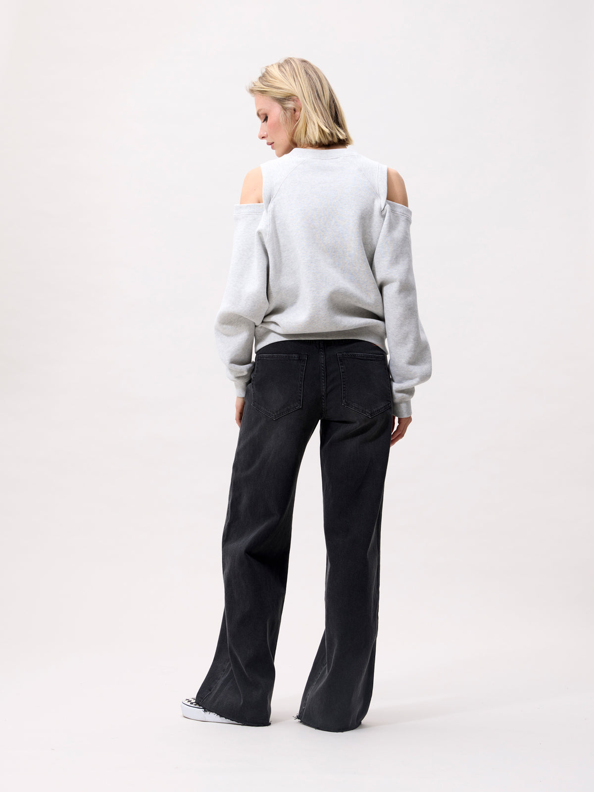 model draagt lichtgrijze sweater met cut outs, achterkant gecombineerd met zwarte wide-leg jeans