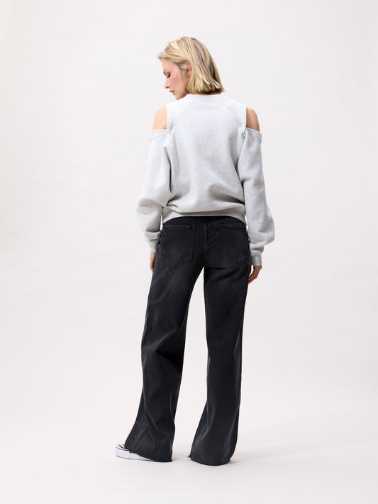 model draagt lichtgrijze sweater met cut outs, achterkant gecombineerd met zwarte wide-leg jeans
