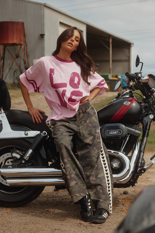 sabbi the raving heart pants camo, model leunt tegen motor met roze oversized shirt