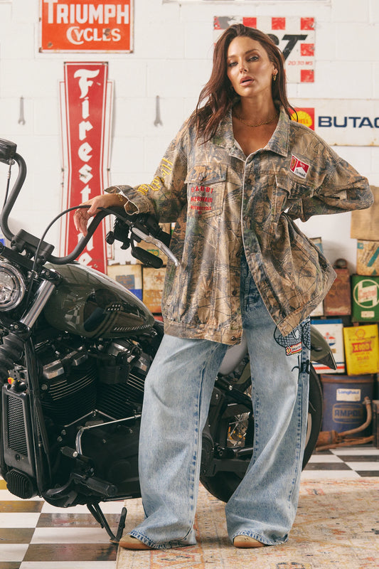 model staat bij motor in oversized camo jasje gecombineerd met wijde jeans