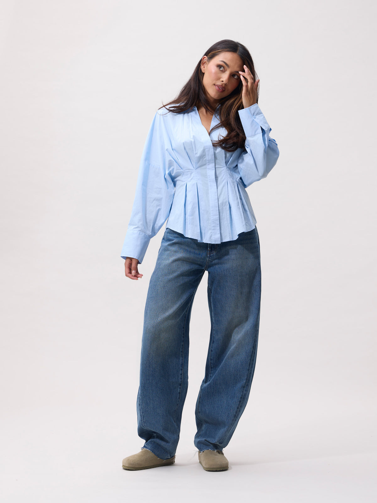 model in lichtblauwe getailleerde blouse gecombineerd met baggy spijkerbroek, vooraanzicht