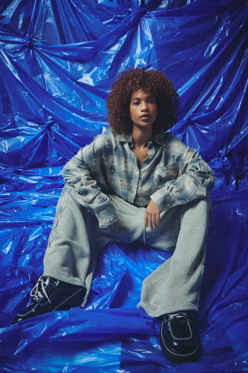 model zit neer in het overshirt, gecombineerd met bijpassende sweatpants