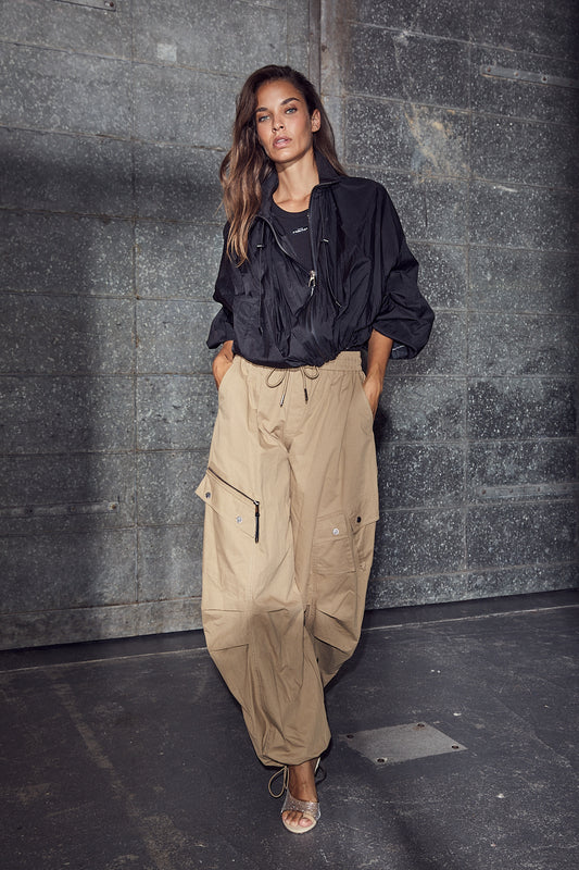 model draagt haute l'amitié iron paper jacket black, gecombineerd met beige cargobroek