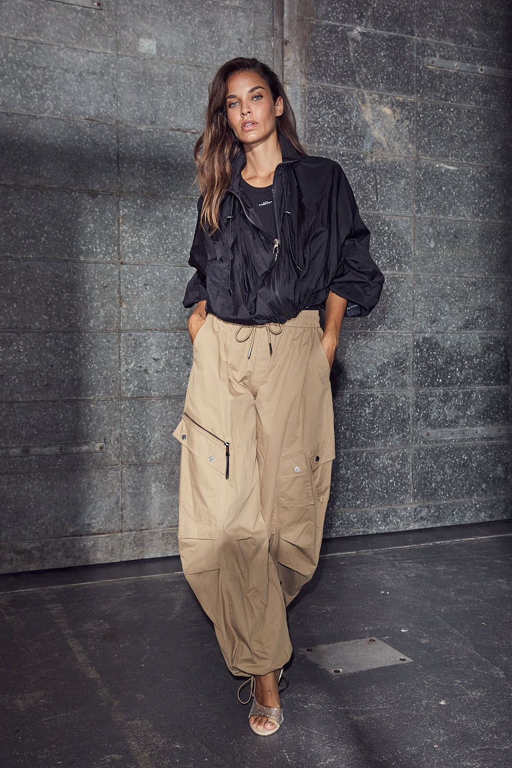 model draagt haute l'amitié air zip tall pant walnut, gecombineerd met zwarte jas